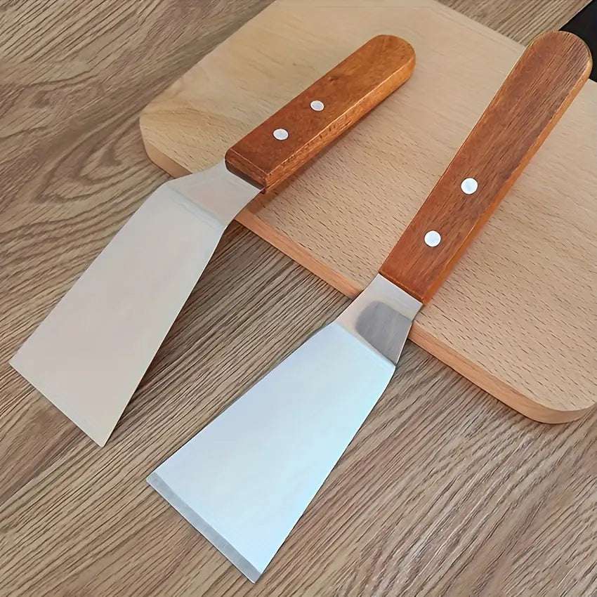 Deux spatules de cuisine avec lames en acier inoxydable et manches en bois posées sur une planche en bois clair.
