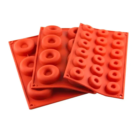 Trois moules en silicone rouge avec plusieurs cavités circulaires pour préparer des mini-donuts.