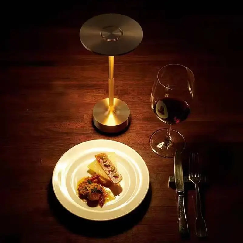 Lampe de table or rechargeable dans un repas avec un verre de vin rouger et une assiette gastronomique