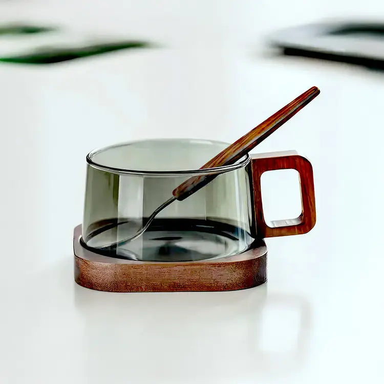 Tasse à café en verre borosilicate foncé avec poignée en bois, posée sur un socle en bois