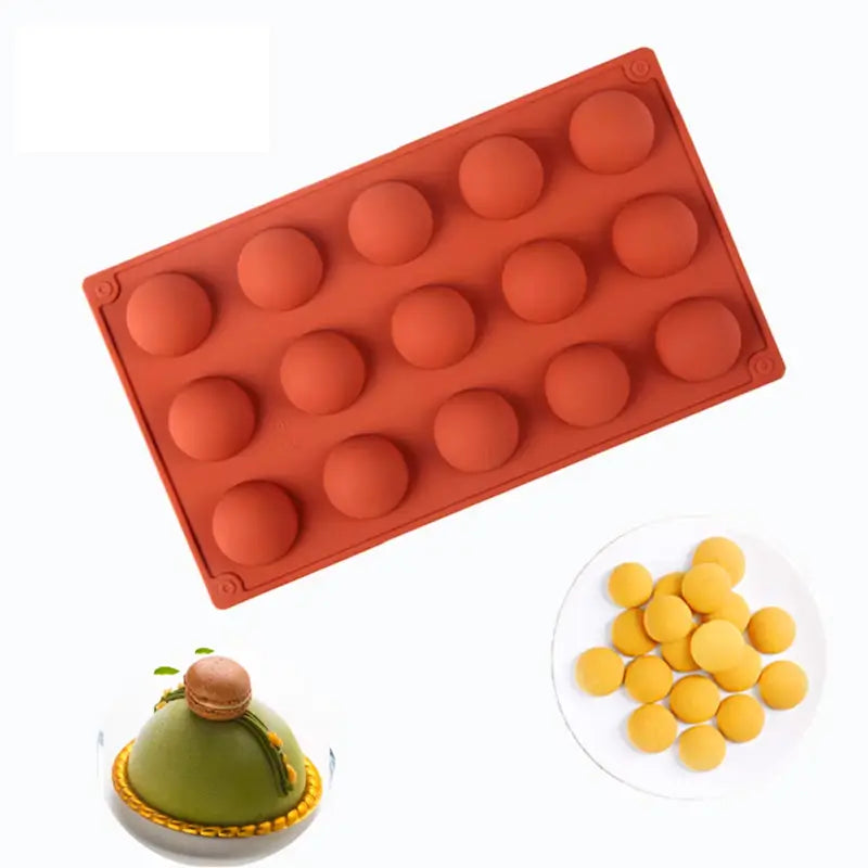 Moule en silicone rouge à 15 cavités demi-sphériques accompagné de desserts finis, dont des petits gâteaux jaunes et un dessert vert décoré.